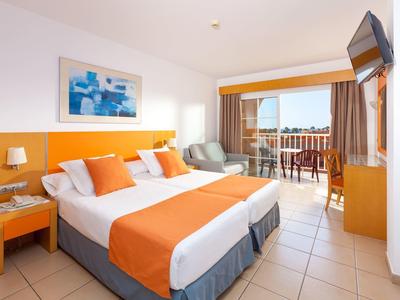 Helles Hotelzimmer mit Doppelbett, orangefarbenen Akzenten, Balkon und Meerblick.