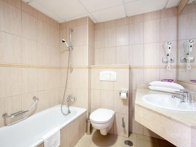 Kleines Badezimmer mit Badewanne, WC, Waschbecken, Handtüchern und beige gefliesten Wänden.