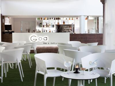 Helles, modernes Café mit weißen Stühlen und Tischen auf grünem Boden und einer Bar im Hintergrund.