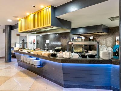 Moderne Bar mit blauer Beleuchtung, Kaffeemaschine und abgedeckten Speisen in hellen Innenräumen.