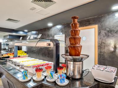 Buffet mit Schokoladenbrunnen, Gläsern, Schalen und diverses Dessert in einem modernen Raum.