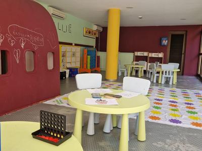 Kinderspielecke mit kleinen Tischen, Stühlen, buntem Teppich und Spielbrett in hellem Raum.