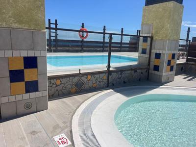 Zwei Schwimmbecken auf Dach mit blauem Himmel, Fliesen und schwarzem Metallgeländer.