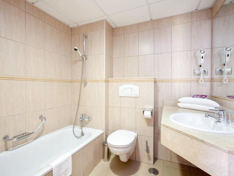 Kleines Badezimmer mit Badewanne, WC, Waschbecken, Handtüchern und beige gefliesten Wänden.