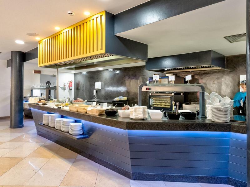 Moderne Bar mit blauer Beleuchtung, Kaffeemaschine und abgedeckten Speisen in hellen Innenräumen.