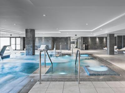 Moderner Wellnesspool mit Wasserfällen, Whirlpools und Liegestühlen in einem eleganten Innenraum.