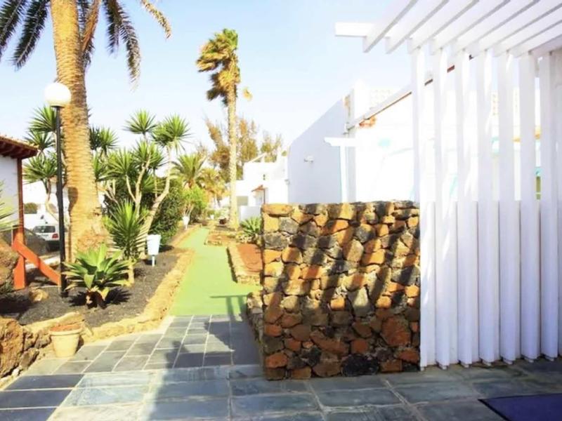 Bright pathway in tropical garden with palm trees and white building beside blue sign.