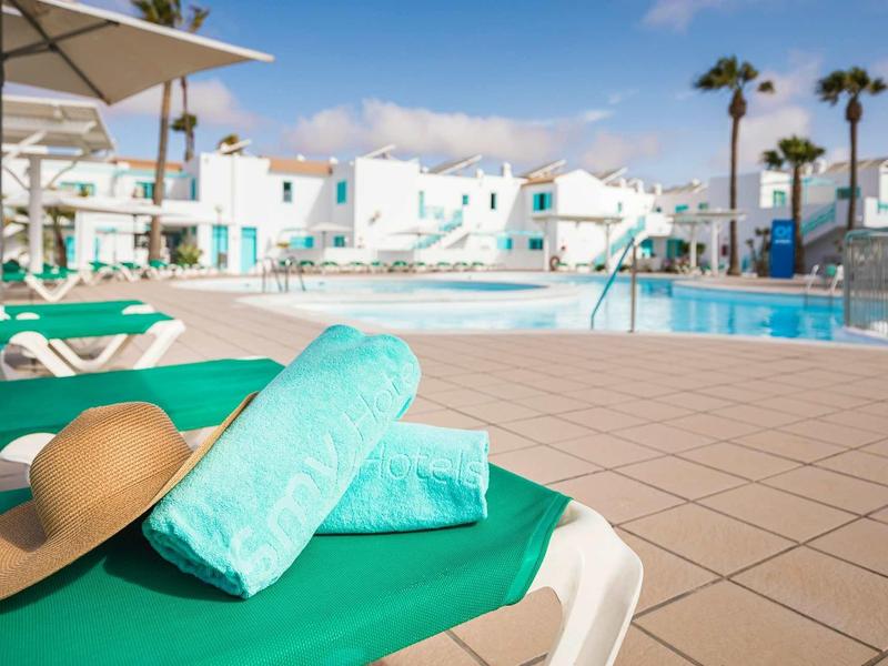 Swimming pool with loungers, towels, and a sun hat at a sunny hotel resort.