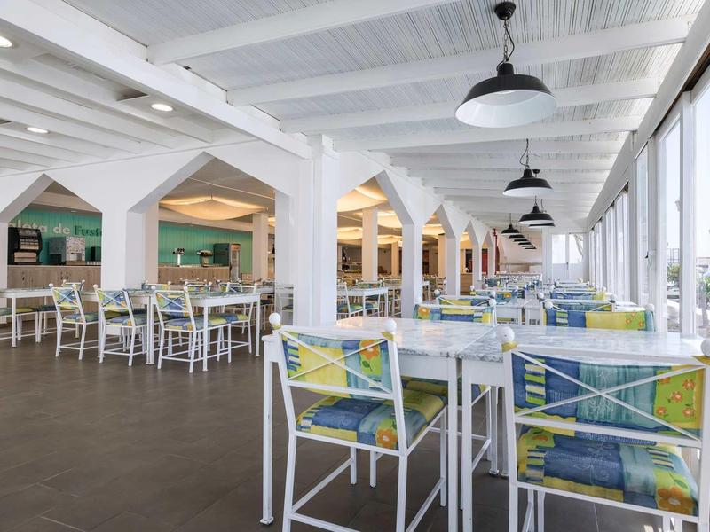 Bright hotel lounge with white ceiling beams and colorful chairs beside large windows.