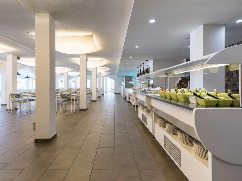 Modern, spacious buffet restaurant with white tables and chairs and a long serving area.
