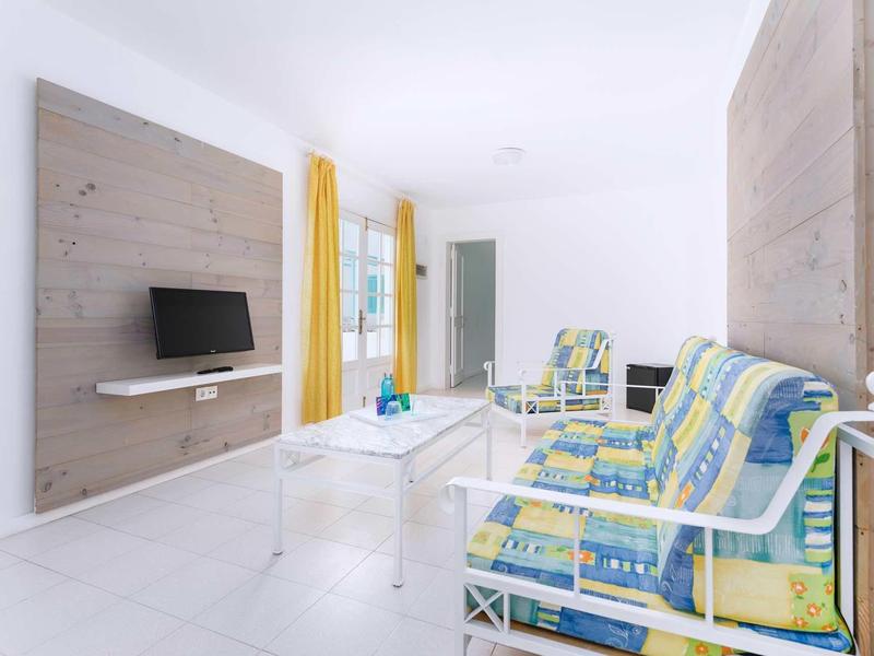 Bright living room with patterned armchairs and wall-mounted TV on wood panels.