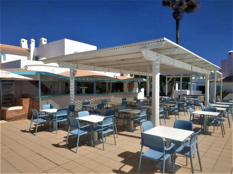 Outdoor restaurant with blue chairs and white tables under sunshade on clear day