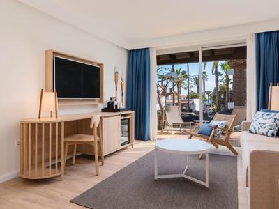 Bright, modern living room with seating, desk, and terrace access with garden view.