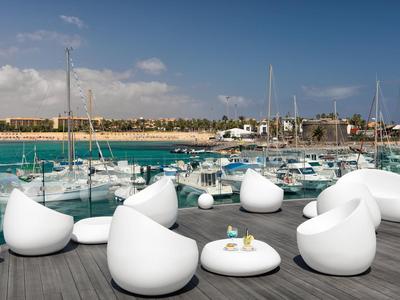White modern outdoor furniture set on terrace overlooking marina and boats under sunny sky.