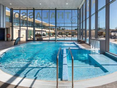 Modern indoor pool with large glass windows overlooking terrace and sea.