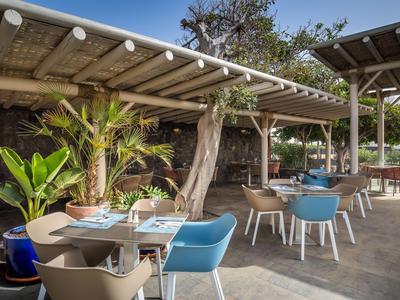 Terrasse mit modernen Tischen, Stühlen und Pflanzen unter einem überdachten Bereich im Freien.