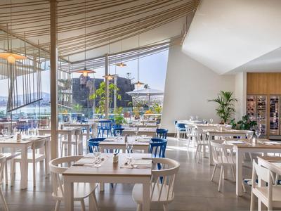 Bright modern breakfast room with white and blue chairs and large windows offering an outdoor view.