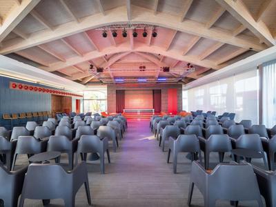 Large conference room with many black chairs and a stage at the end.