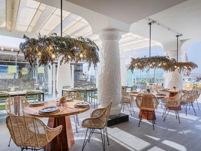 Bright restaurant with wooden tables, wicker chairs, decorated chandeliers, plenty of daylight.