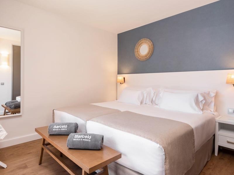 Modern hotel room with large bed, dark blue wall, and wooden furniture.