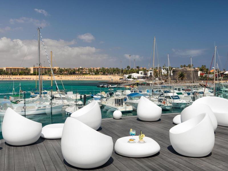 White modern outdoor furniture set on terrace overlooking marina and boats under sunny sky.