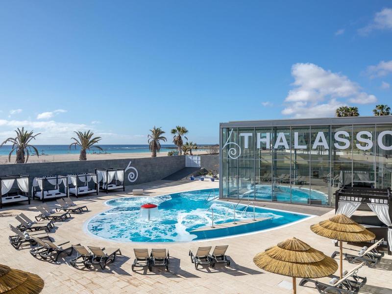Outdoor pool with lounge chairs, sun umbrellas, and Thalasso spa by the sea.