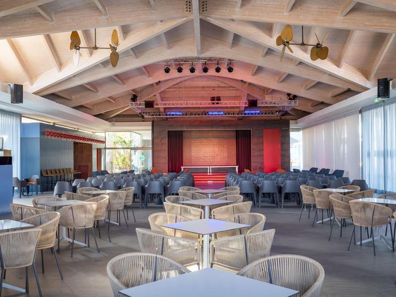 Large dining hall with modern tables and chairs and a stage at the far end.