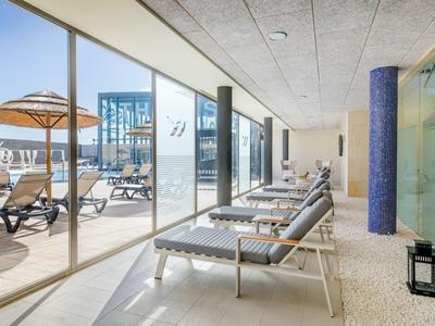 Moderner Wellnessbereich mit Liegen und Blick auf Terrasse mit Sonnenschirmen und Liegestühlen.