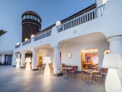 Ein moderner Außenbereich eines Hotels mit weißen Säulen und Sitzbereichen bei Sonnenuntergang.