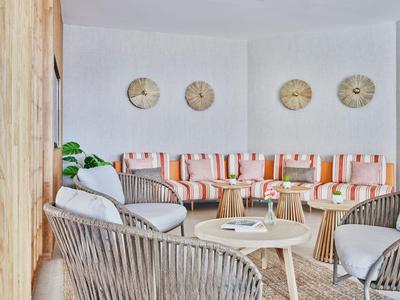 Gemütlicher Wartebereich mit Korbsesseln, buntem Sofa und runden Holztischen.