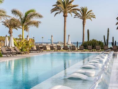 Moderner Außenpool mit Liegen und Palmen, Meer im Hintergrund