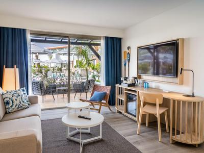 Modern eingerichtetes Hotelzimmer mit Terrasse, Sofa, Fernseher und Schreibtisch.