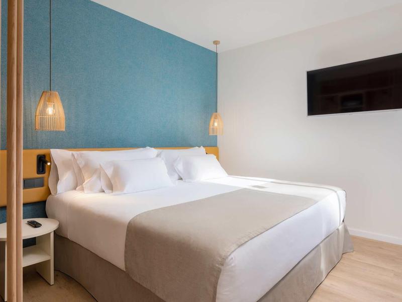 Modernes Schlafzimmer mit großem Bett, blauer Wand, Holzboden und Wandfernseher.