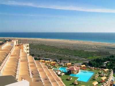 Blick auf ein Hotel mit Poolanlage und Strand im Hintergrund an der Küste.