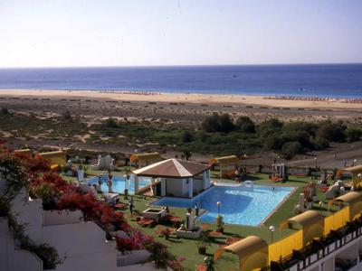 Pool area with sun umbrellas and a wide beach and sea view.