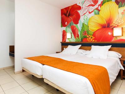 Hotel room with large beds, orange runners, and colorful floral wallpaper.