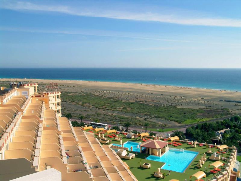 Hotel with large pools and a view of the sea and beach in the background.