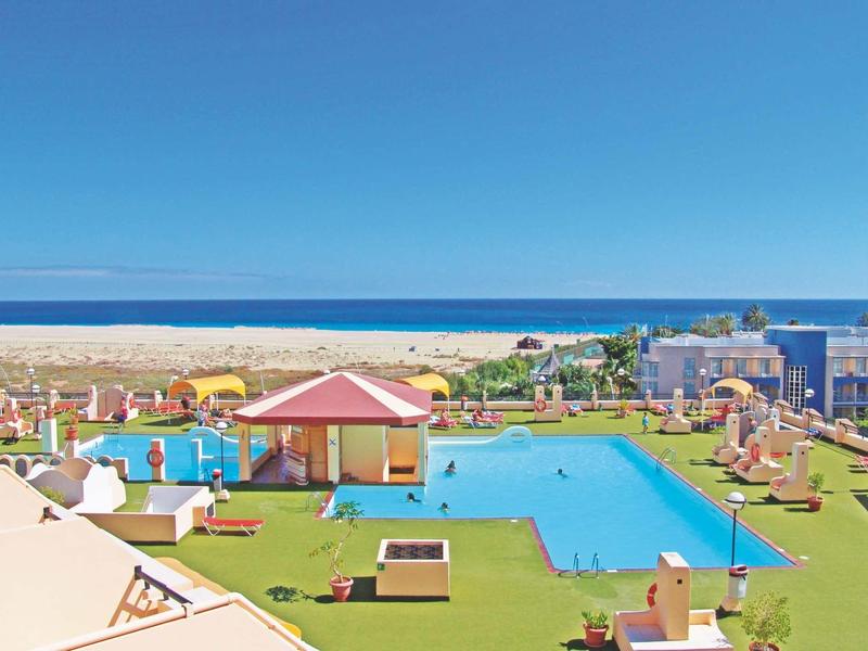 Large pool area with sun loungers, umbrellas, and a clear sky view of the sea.
