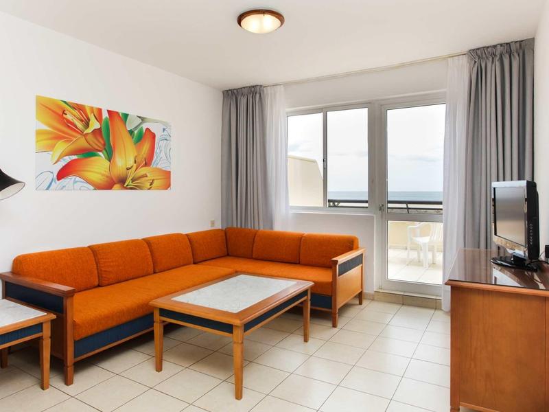 Modern living room with orange corner sofa, coffee table, and balcony access.