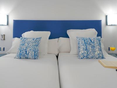 Modern hotel room with two single beds, blue headboards, and white walls