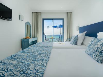 Brightly furnished hotel room with two beds and balcony with sea view