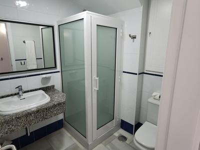 Compact hotel bathroom with shower, toilet, sink, and large mirror above granite countertop.
