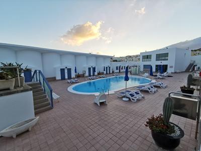 Outdoor hotel pool area with sun loungers, umbrellas, and white buildings under a clear sky.