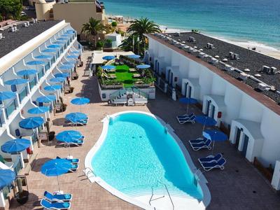 Aerial view of a hotel pool area with blue lounge chairs, umbrellas, and ocean in the background.