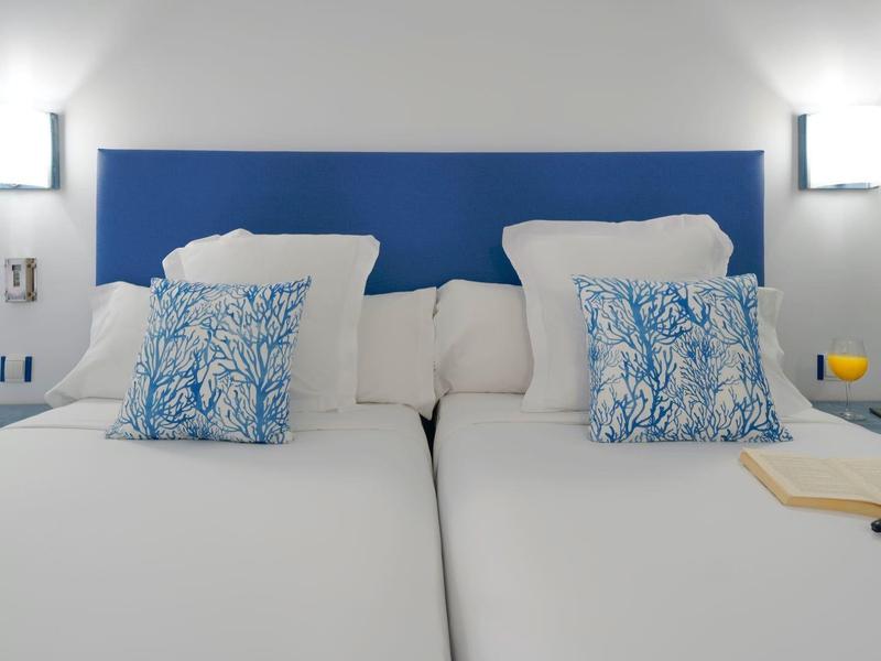 Modern hotel room with two single beds, blue headboards, and white walls