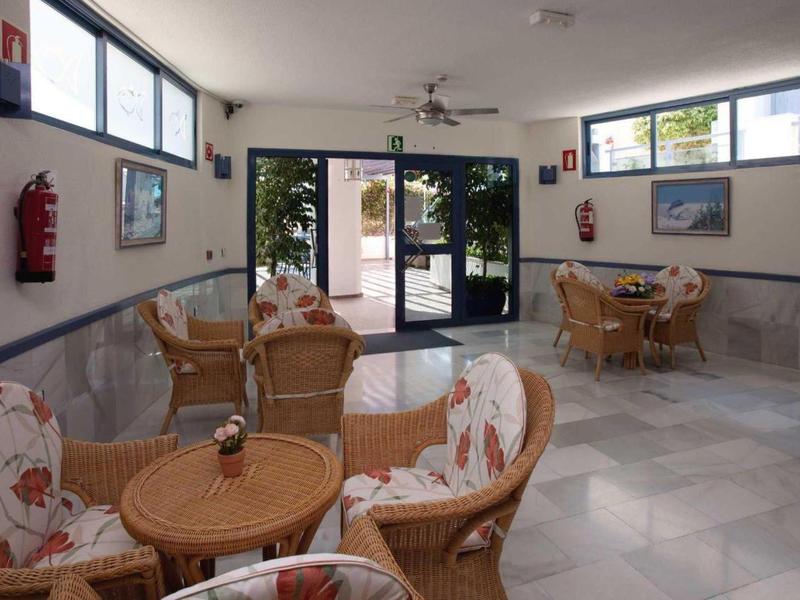 Cozy seating area with wicker chairs and round tables in a bright indoor space with large windows.
