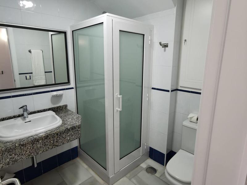 Compact hotel bathroom with shower, toilet, sink, and large mirror above granite countertop.