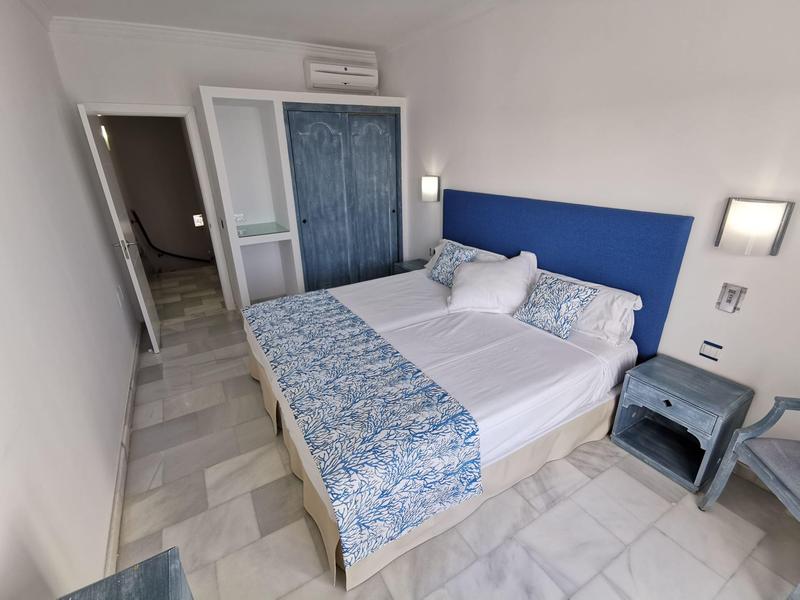 Modern hotel room with a double bed, blue headboard, nightstand, and tiled floor.