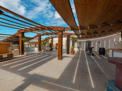 Ampia terrazza con tetto in legno e ombre solari sotto un cielo blu