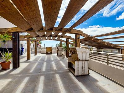 Area aperta sul tetto con travi in legno, posti a sedere e vista sul mare in una giornata di sole.